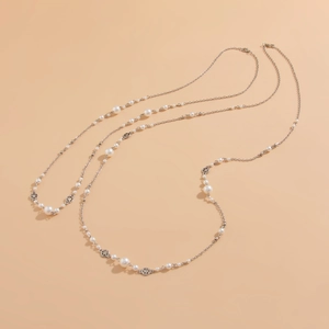 Detail of long pearl necklace with silver flower charms on warm beige background