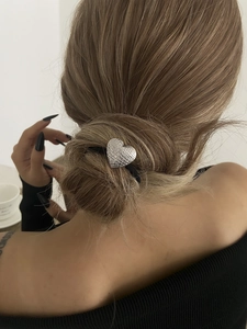 Détail de l'élastique à cheveux en métal argenté en forme de cœur sur un chignon bas