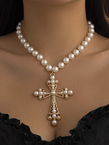 Detail of baroque pearl necklace with an ornate gold cross pendant on a model