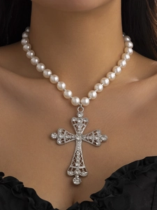 Close-up of pearl necklace featuring a large ornate silver cross pendant with rhinestones