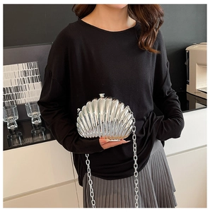 Detailed view of silver shell-shaped evening bag with glossy metal finish and chain strap
