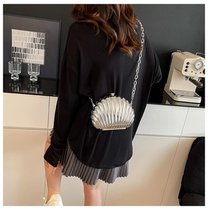 Detail of silver shell-shaped metallic chain bag worn by model in a stylish interior