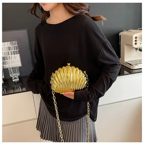 Detail of a golden shell-shaped clutch with metallic texture and a thick chain strap