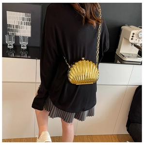 Golden shell-shaped evening bag with metallic finish and chain strap worn by a model