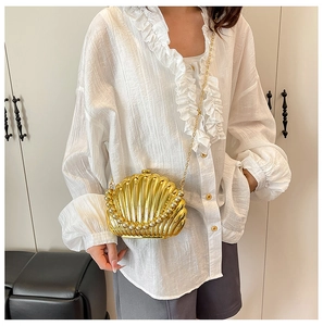 Close-up of golden shell-shaped evening clutch bag with pearl inlay and chain strap