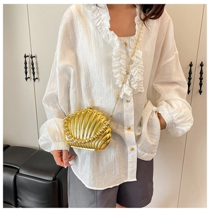 Detailed view of a gold shell-shaped clutch bag with pearl trim and gold chain on a model