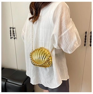 Detail of a golden shell-shaped clutch bag with beaded edges and metallic chain strap