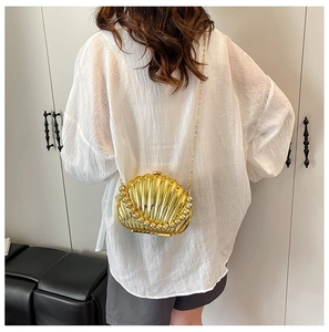 Detail of a shell-shaped gold evening clutch bag with chain strap worn by a model
