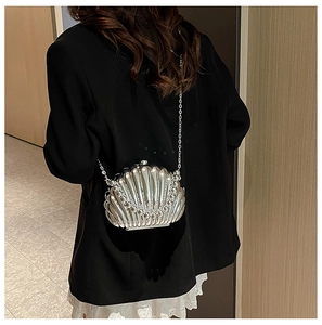 Detail of silver shell-shaped evening bag with metallic texture and chain strap