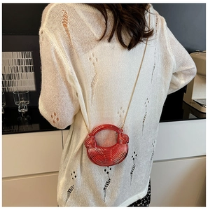 Rote Halbmondtasche mit Spiralstruktur und Goldkette auf weißem Strickpullover