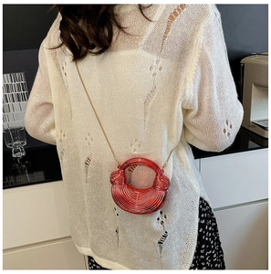 Detail einer hellroten Halbmondtasche mit Goldkette auf einem weißen Strickpullover