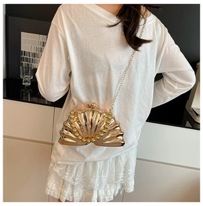 Détail de pochette de soirée dorée en forme de coquillage avec poignée perle