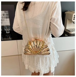 Pochette coquillage dorée avec poignée en perles et chaîne portée par un mannequin