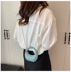 Close-up of light blue mini bag with twisted handle and gold chain strap worn cross-body