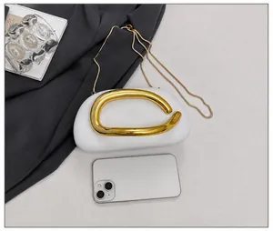 Detalle de bolso blanco con asa dorada y móvil para comparar el tamaño del producto