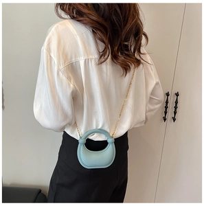 Rear view of a light blue crescent shoulder bag with golden chain strap on a model