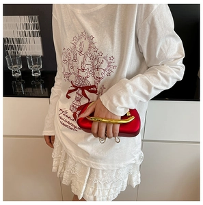 Detail of red metallic handle clutch bag paired with a white artistic candle print shirt
