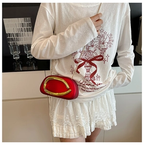Detail of red acrylic clutch with golden oval metal accent and slim chain strap