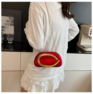 Detail of red acrylic evening clutch bag with gold C-shaped metal decoration and chain strap