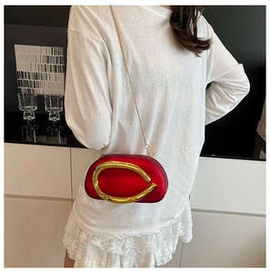 Model showing red oval clutch bag with gold abstract metal accent and chain strap
