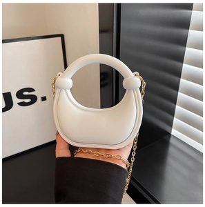 Detail of white half-moon handbag with round handle and detachable gold chain strap