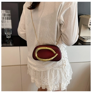 Close-up of burgundy hardshell evening bag with golden C-shaped metal clasp and chain