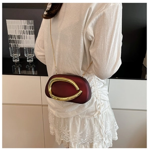 Detail of burgundy clutch with large gold U-shaped buckle and fine metal chain strap