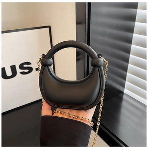 Close-up of black mini semi-circular handbag with round handle and gold chain strap