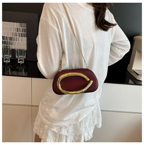 Detail of burgundy leather evening bag with large gold C-clasp and metallic chain strap