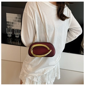 Burgundy hard shell evening clutch with gold C-handle and chain strap on a model