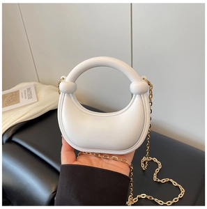 Detail of a white crescent handbag with gold chain strap and ring handle in a chic setting