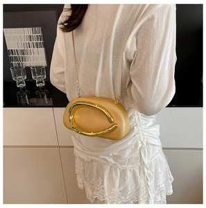 Detail of apricot acrylic evening clutch featuring a gold circular metal buckle and chain