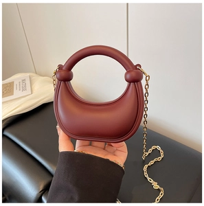 Detailed view of burgundy crescent handbag with round handle and gold chain strap