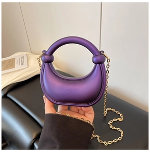Detail of a dark purple half-moon handbag with round handle and gold chain strap