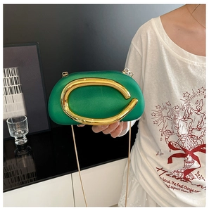 Detail of emerald green hard shell clutch bag featuring a polished gold metallic handle