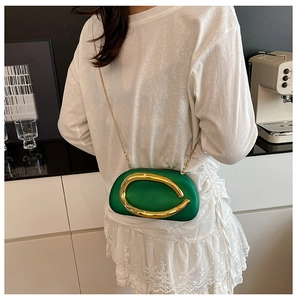 Detail of emerald green hard-shell bag featuring a large C-shaped gold metal clasp