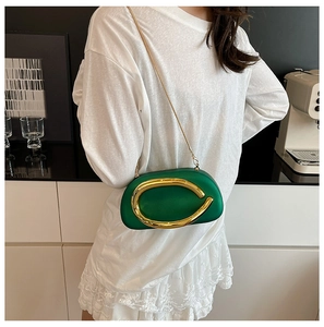 Detail view of emerald green hard shell clutch bag with gold horseshoe buckle and chain