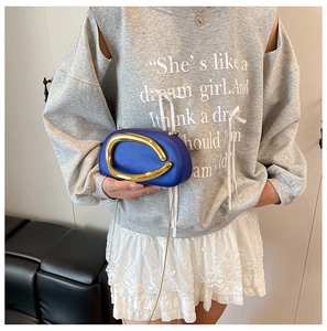 Detail of royal blue oval clutch featuring a gold circular handle and fine chain strap