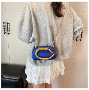 Blue acrylic clutch bag with large gold metal ring and chain strap worn by a model