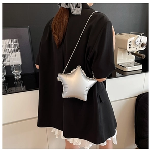 Detail of silver star-shaped crossbody bag worn over a black blazer in a cafe