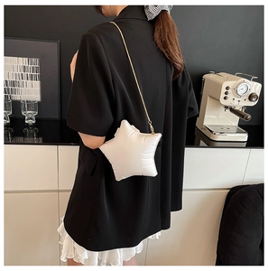 Detail of white quilted star crossbody bag with gold chain on a black blazer