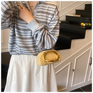 Detail of beige pleated cloud bag with oversized gold C-shaped metal handle and chain strap
