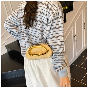 Detail of champagne shell clutch featuring a gold curved handle and slim chain strap