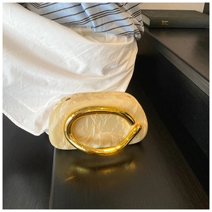 Close-up of cream acrylic evening bag with marble texture and golden metal handle