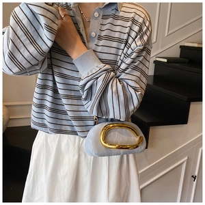 Close-up of light blue textured handbag with oversized golden C-shaped metal handle