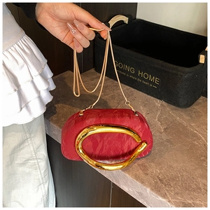Detail of red pleated fabric evening bag with oversized gold C-shaped metal handle