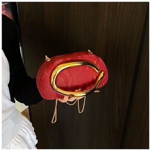 Detail of red clutch bag with large gold metal oval handle and chic chain strap