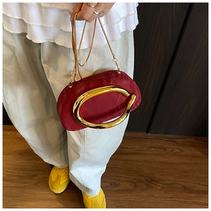 Detail of burgundy acrylic clutch with gold ring handle and chain strap for evening party
