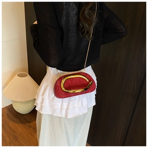 Model wearing a red acrylic clutch with gold ring handle and chain strap against a black dress