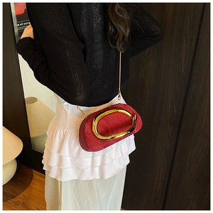 Detail of red satin clutch bag featuring a gold C-shaped metal handle and chain strap